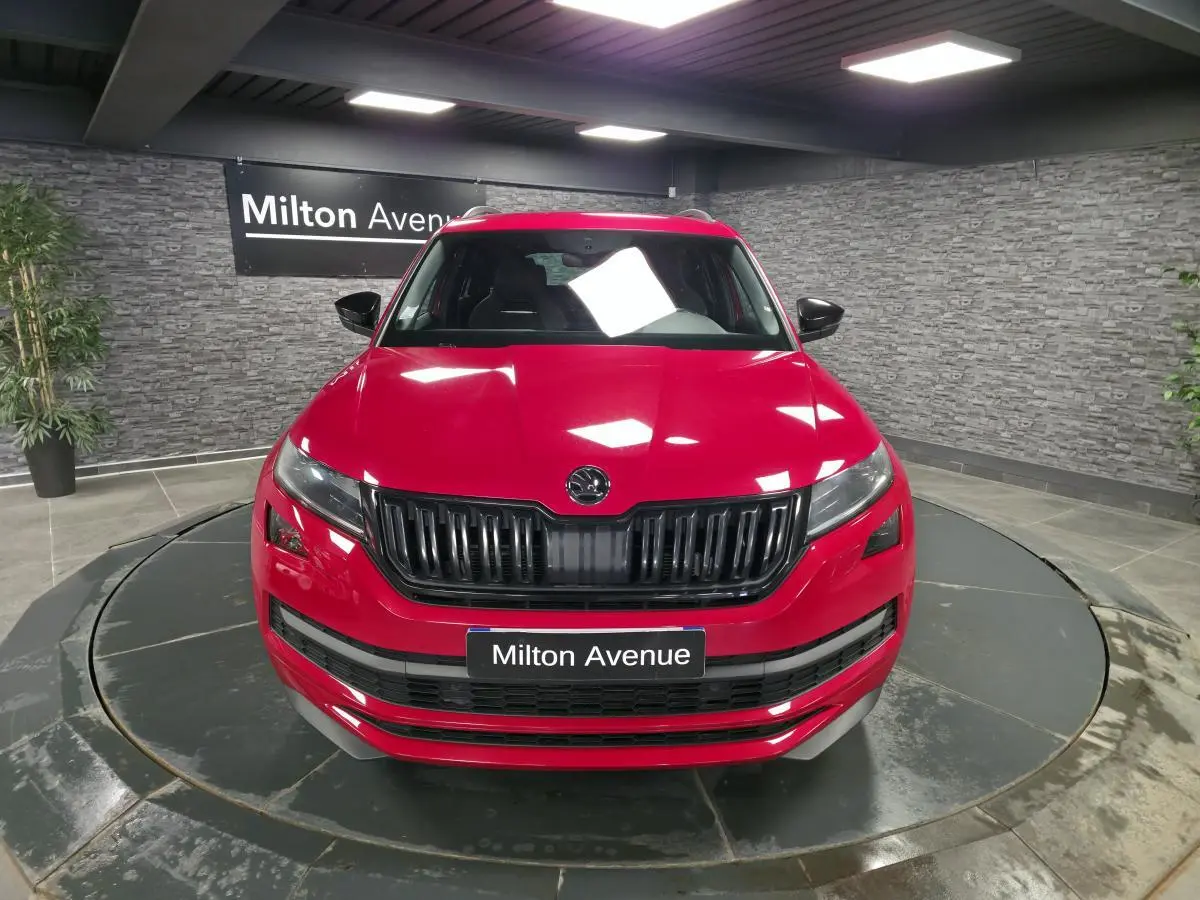 Vue avant d'un Skoda Kodiaq rouge 2021 avec calandre noire et plaque "Milton Avenue" en intérieur showroom.