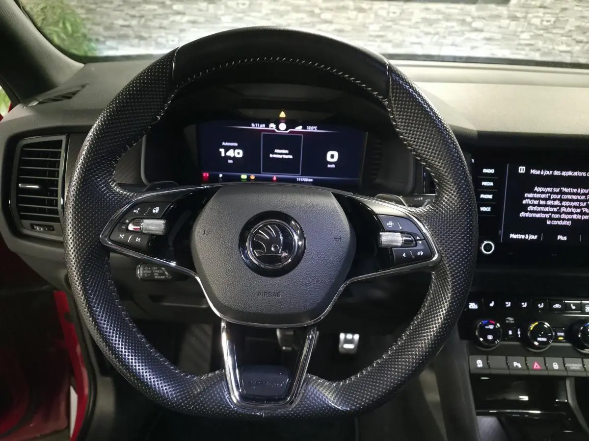 Vue intérieure centrée sur le volant cuir perforé noir du Skoda Kodiaq rouge, avec tableau de bord digital et écran tactile.