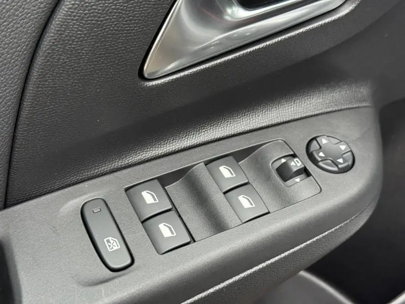 Gros plan sur les commandes de lève-vitres et réglage des rétroviseurs côté conducteur d'une Opel Corsa noire.