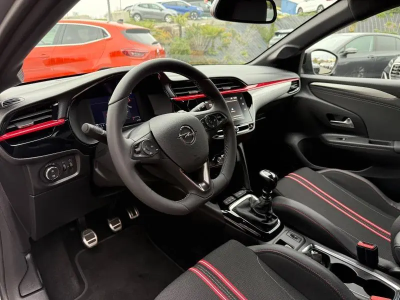 Intérieur noir et rouge de l’Opel Corsa 1.2 Turbo 2023, vue côté conducteur avec volant cuir et levier de vitesse manuel.