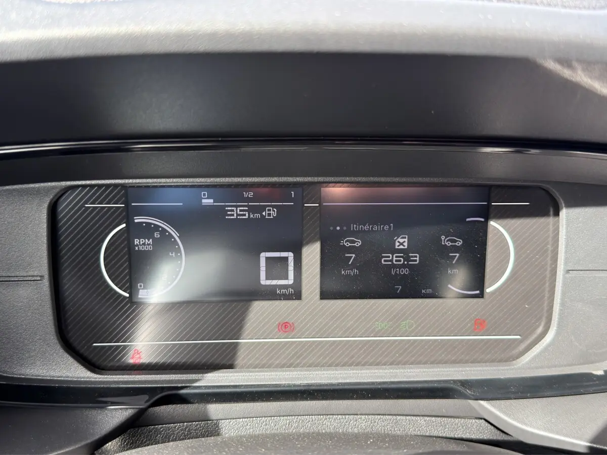 Gros plan sur le combiné d'instruments numérique du Citroën Berlingo blanc, affichant vitesse et consommation.