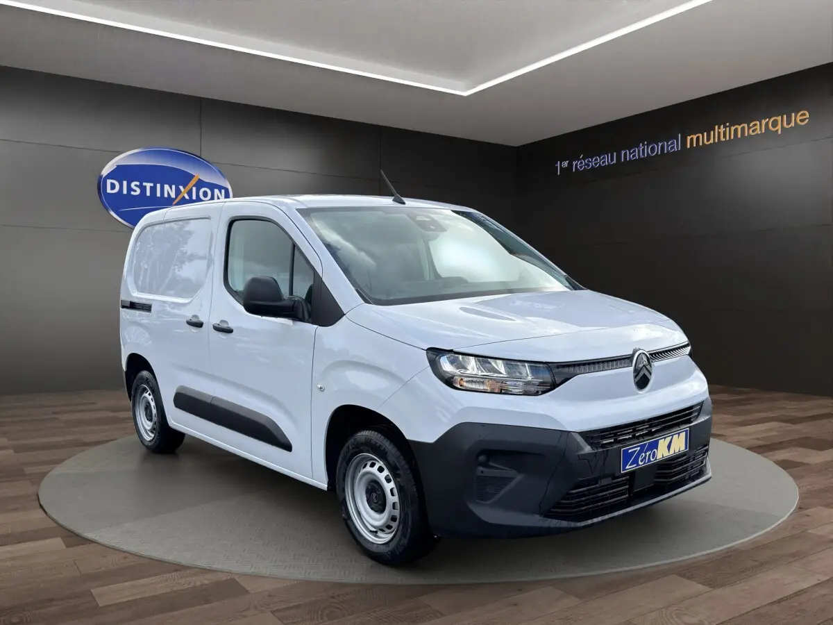 Vue 3/4 avant droit du Citroën Berlingo blanc avec pare-chocs noirs et jantes acier en showroom.