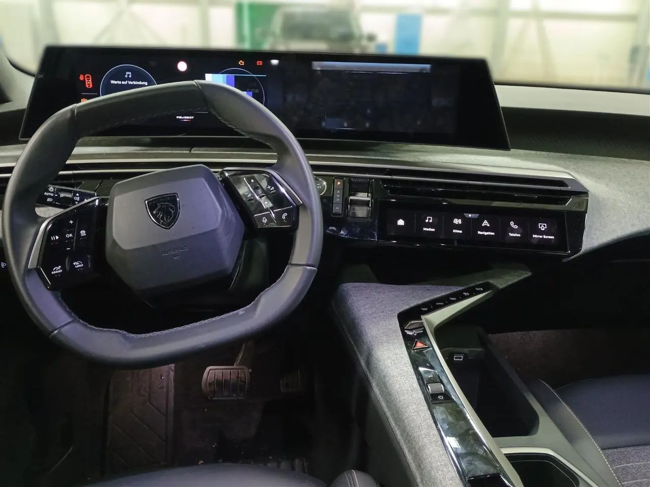 Vue intérieure du poste de conduite du Peugeot 3008 Hybrid 2025 avec volant compact cuir noir et écran panoramique incurvé.