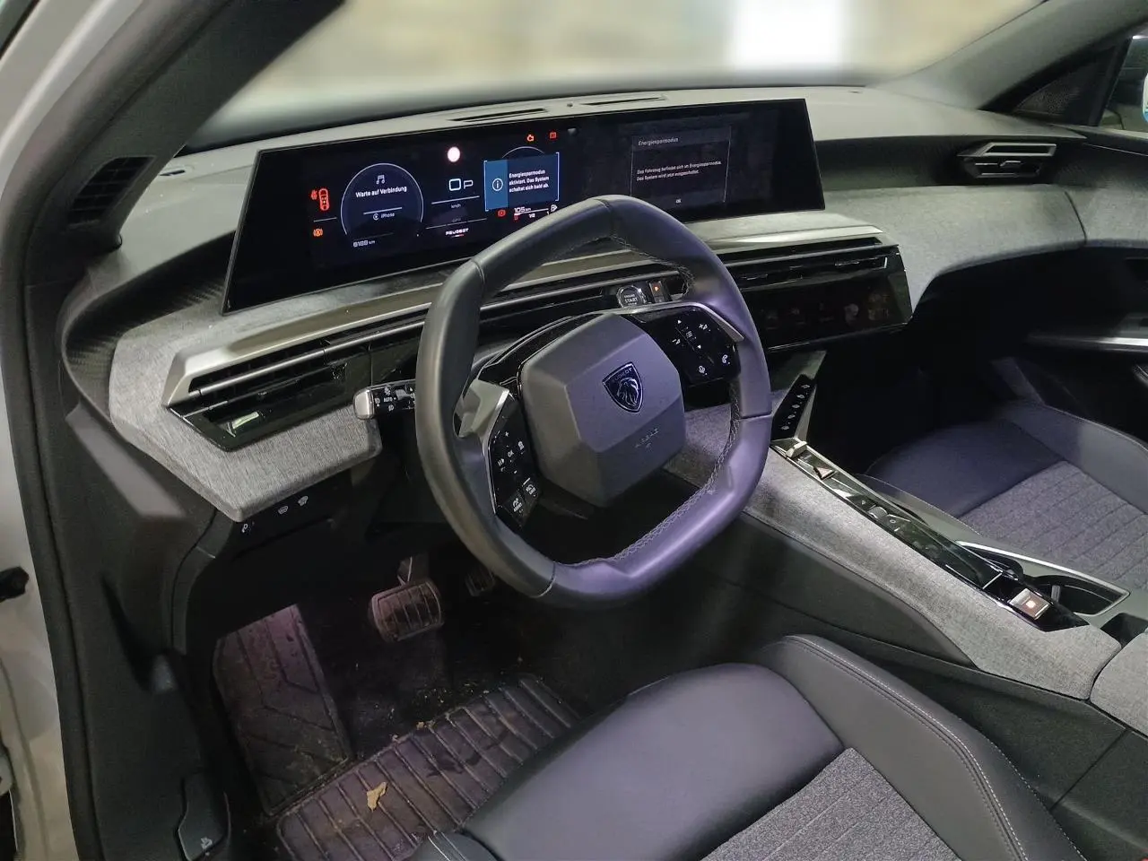 Vue intérieure côté conducteur du Peugeot 3008 Hybrid 2025, volant compact cuir noir et tableau de bord numérique panoramique.