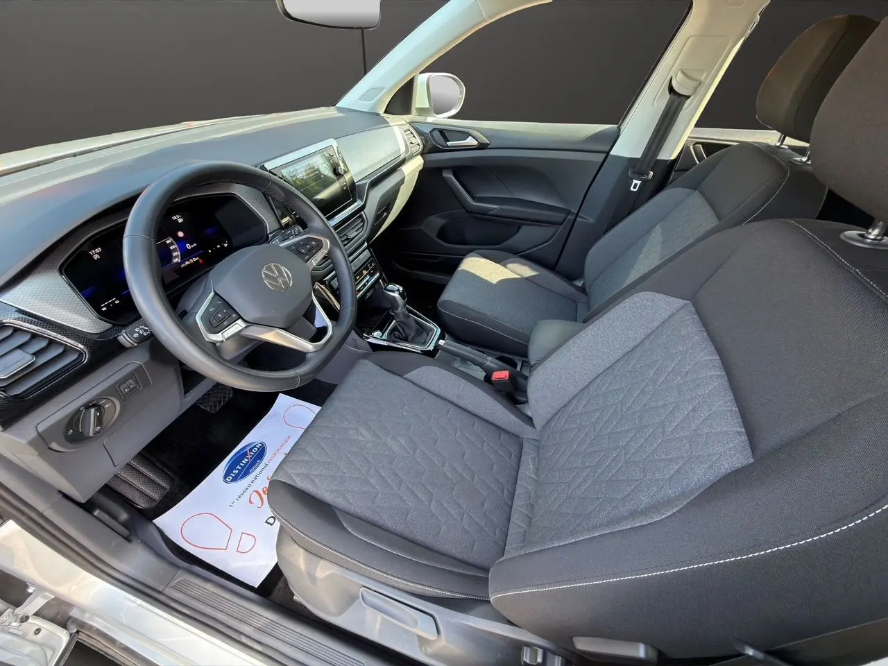 Vue intérieure côté conducteur du Volkswagen T-Cross 2025, sellerie tissu noir avec tableau de bord moderne.