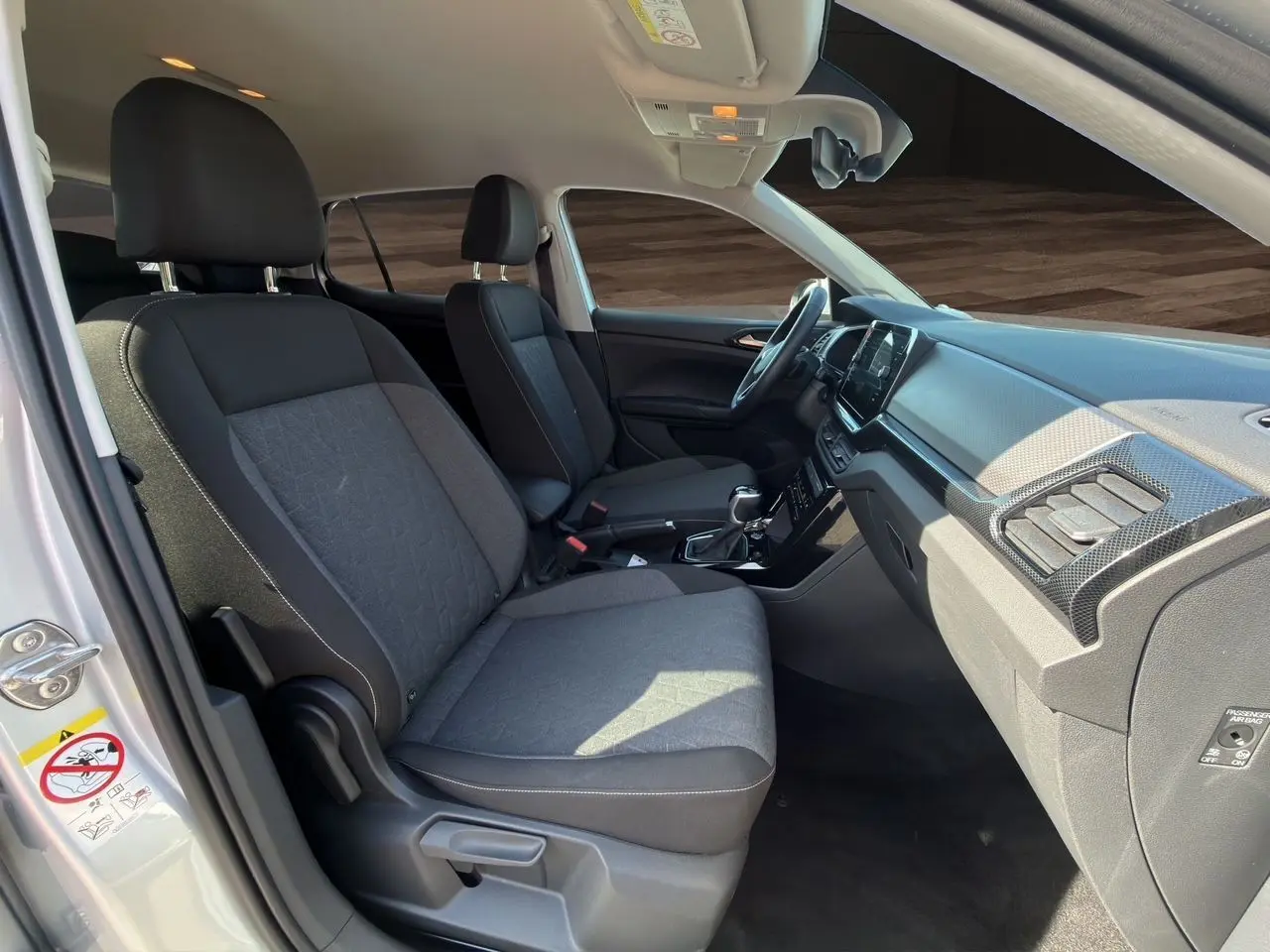 Vue intérieure côté conducteur du Volkswagen T-Cross 2025 argent, sièges tissu noir et tableau de bord moderne.