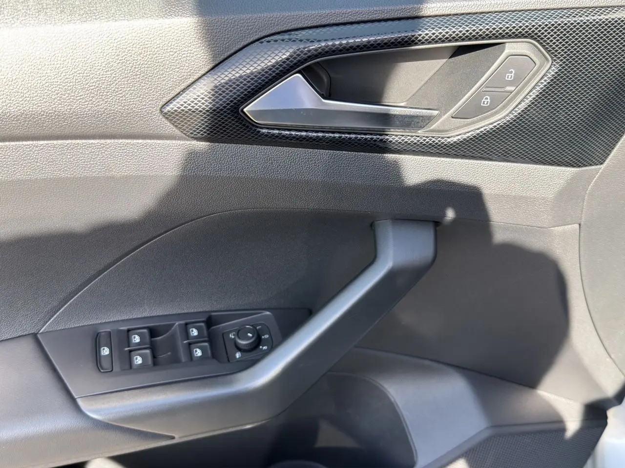 Vue rapprochée de la porte côté gauche du Volkswagen T-Cross 2025 en tissu noir avec commandes électriques et poignée grise.