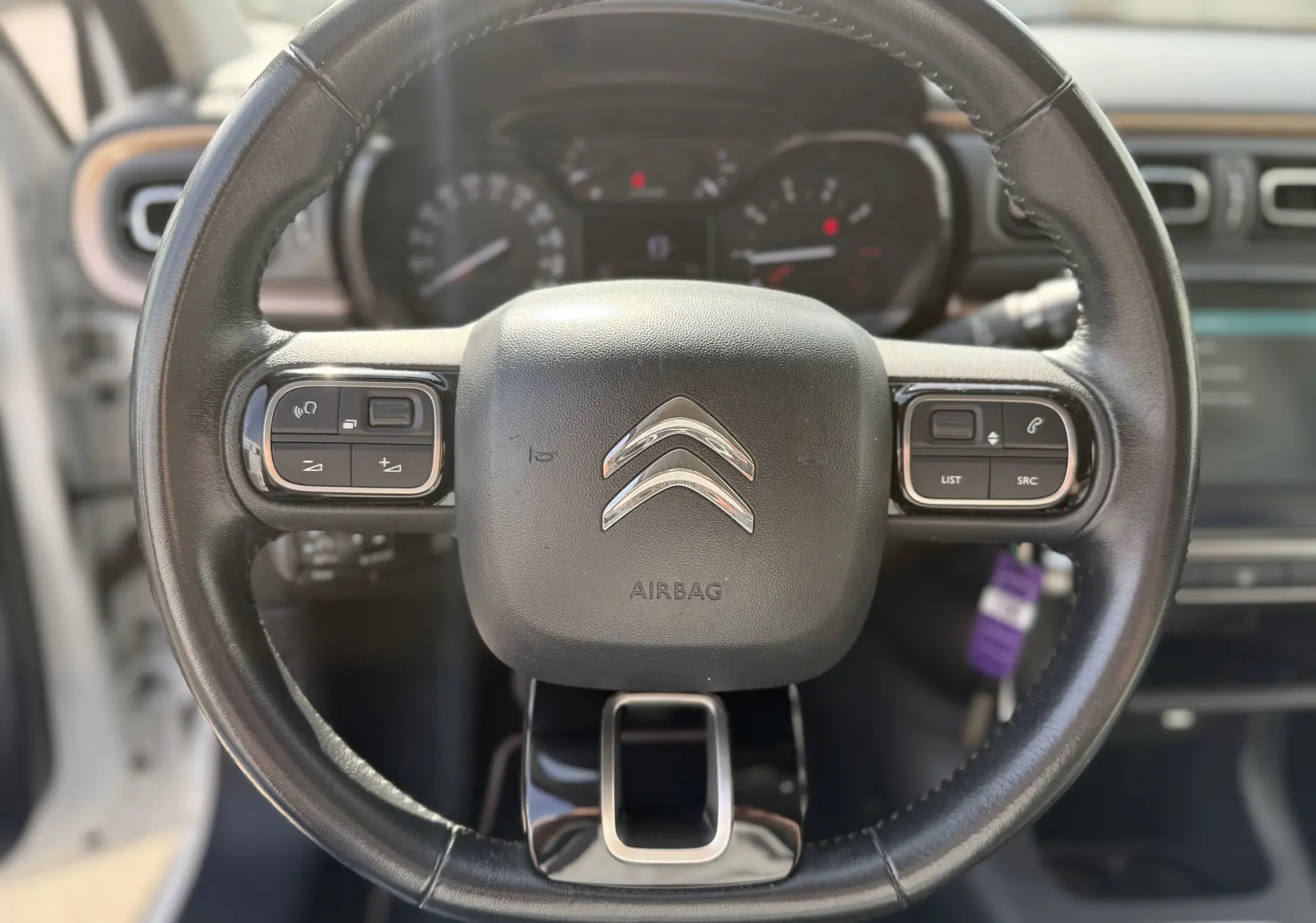 Vue rapprochée du volant noir de la Citroën C3 1.2 PureTech 83 Origins avec commandes intégrées et logo chromé central.