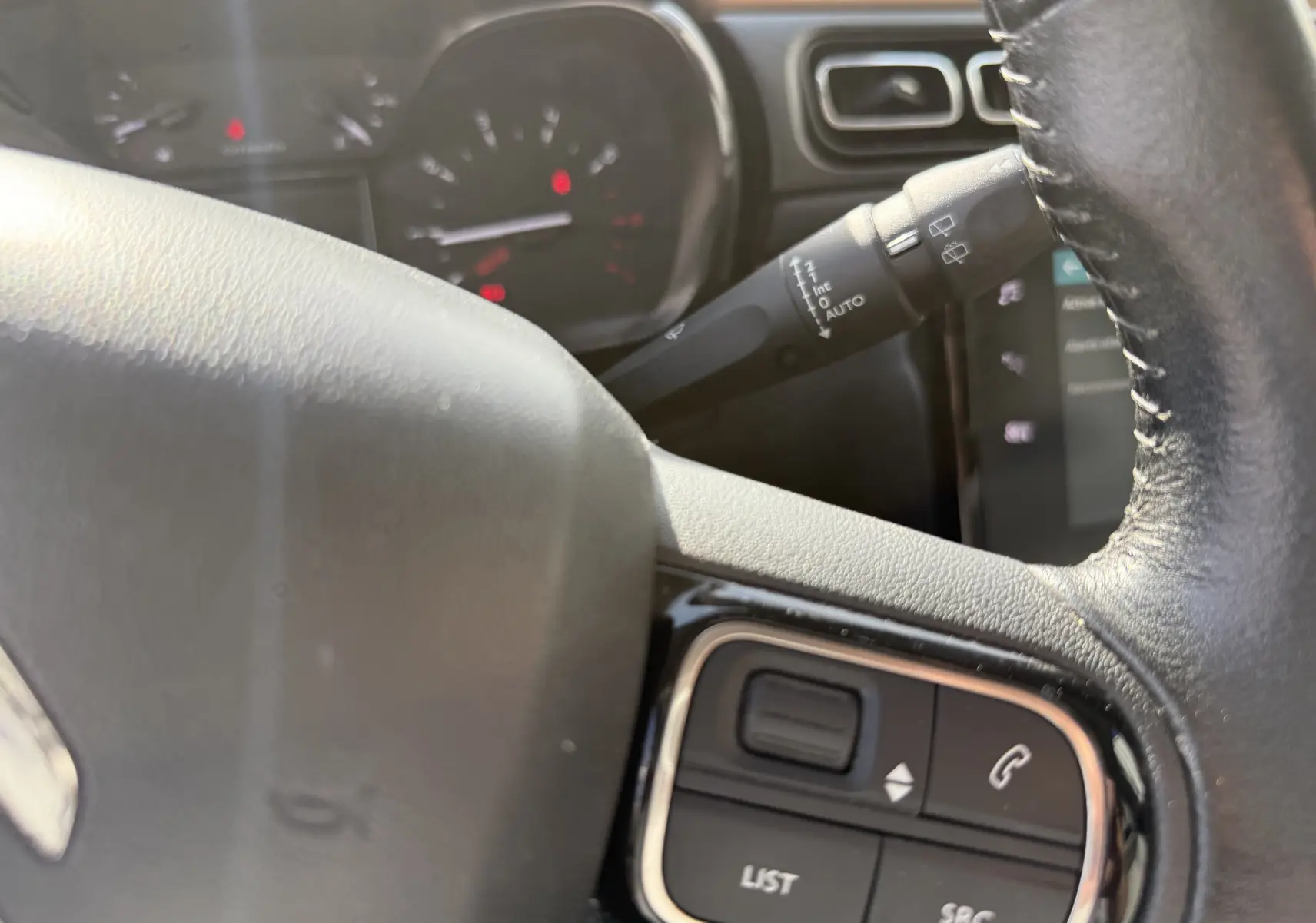 Gros plan sur le volant noir de la Citroën C3 1.2 PureTech 83 Origins, montrant les commandes audio et le commodo d’essuie-glace.