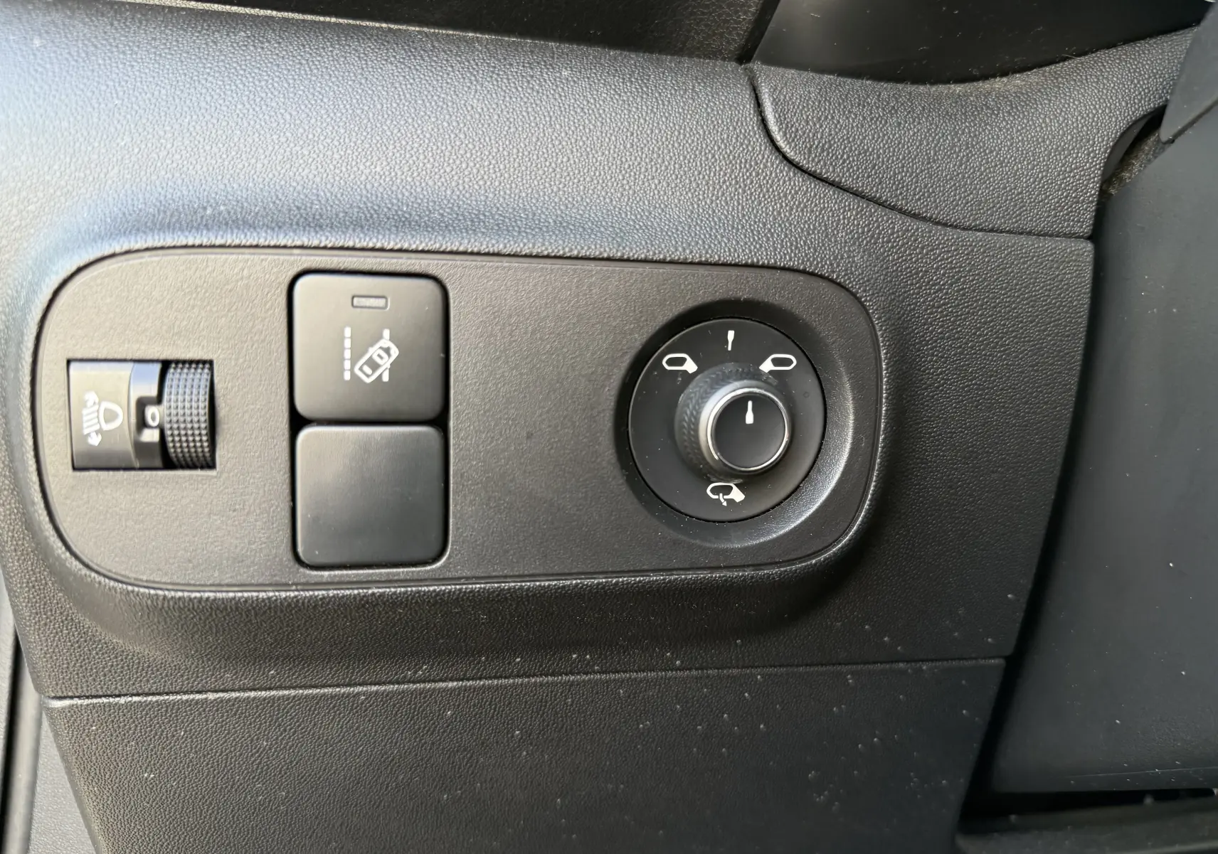 Gros plan sur les commandes noires de réglage des rétroviseurs et des phares côté gauche d'une Citroën C3 blanche toit noir.