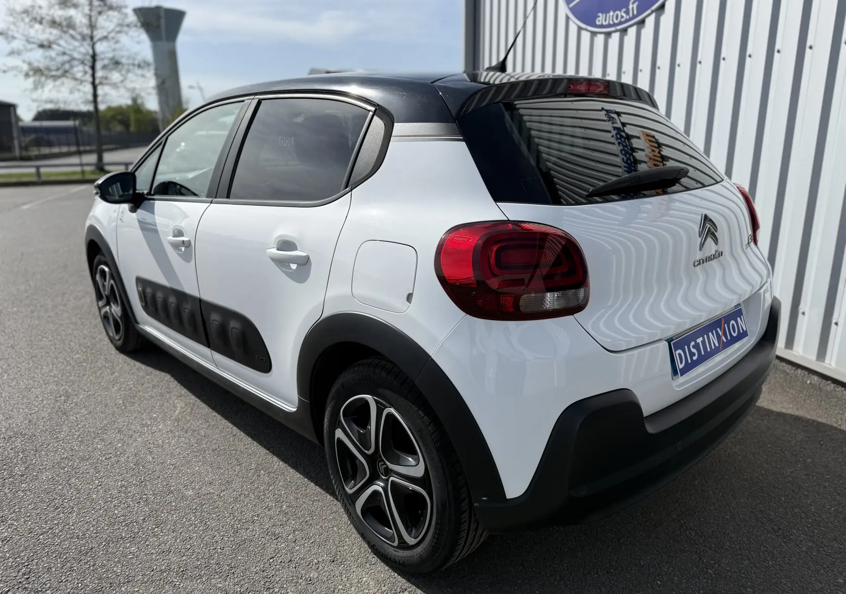 Vue 3/4 arrière droite d'une Citroën C3 blanche au toit noir avec protections latérales noires et jantes stylisées.
