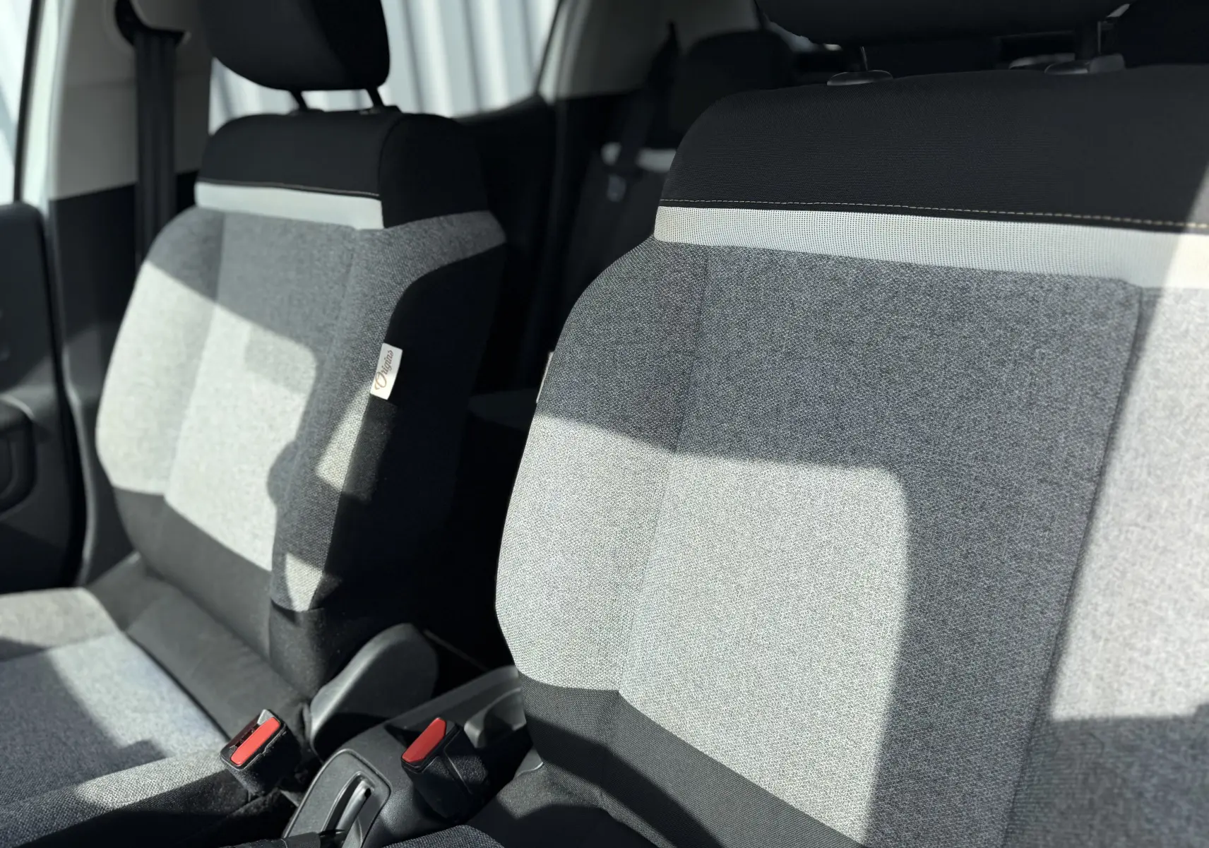 Gros plan sur les sièges avant gris et noirs de la Citroën C3 1.2 PureTech 83 Origins, intérieur lumineux.