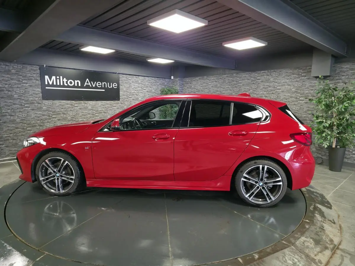 BMW Série 1 116d M Sport rouge vue de profil côté gauche, avec jantes alliage 18 pouces et badge M sur l'aile avant.