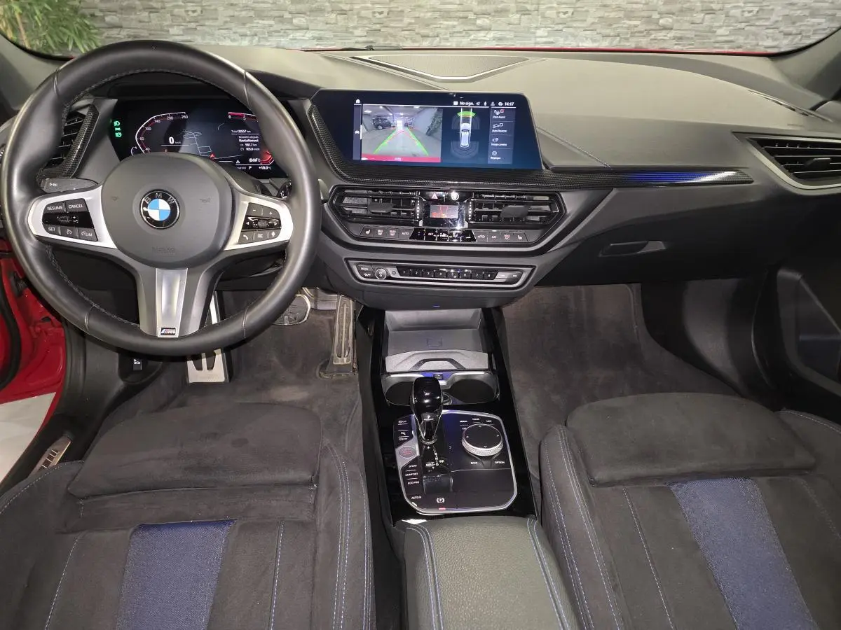 Vue intérieure avant de la BMW Série 1 116d M Sport 2024, sellerie tissu Alcantara noire avec inserts bleus et écran tactile central.