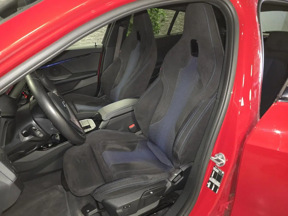 Vue intérieure côté conducteur d'une BMW Série 1 116d rouge avec sièges sport M en tissu et Alcantara noir.