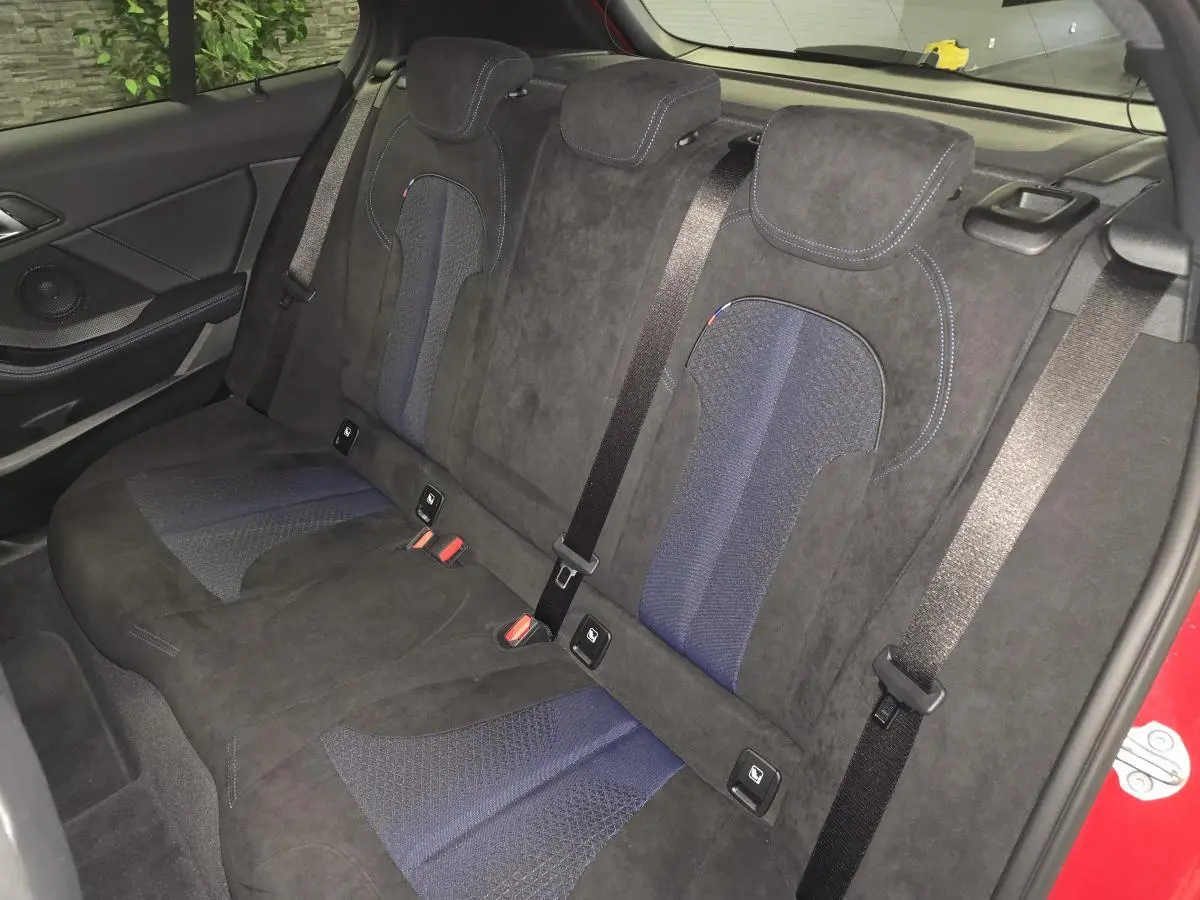 Vue intérieure arrière des sièges en tissu et Alcantara noir et bleu de la BMW Série 1 116d M Sport rouge 2024.