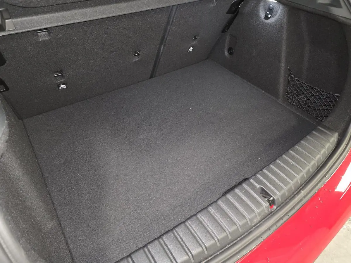 Vue rapprochée du coffre ouvert d'une BMW Série 1 116d M Sport rouge, montrant le tapis et les fixations internes.