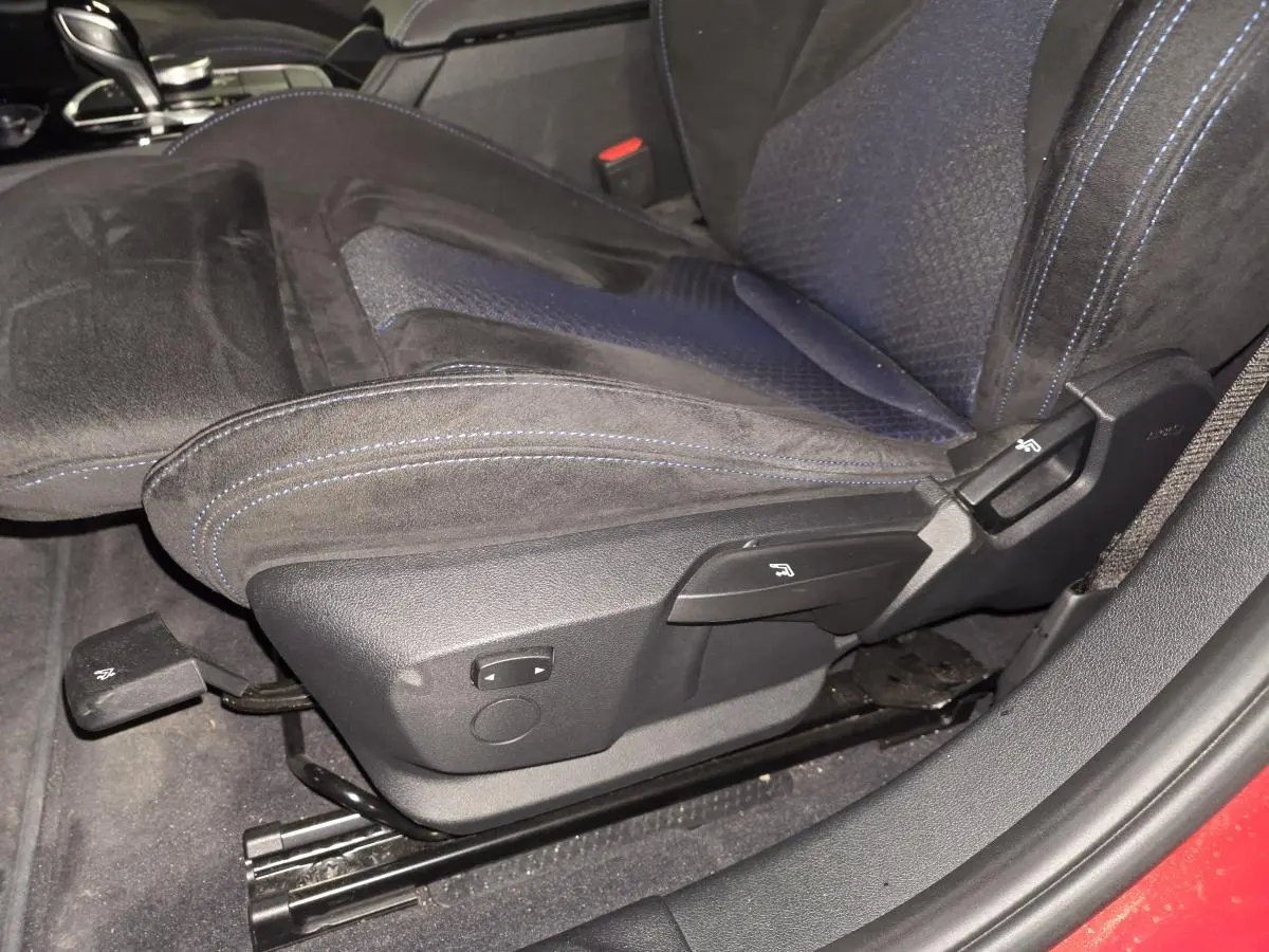Gros plan sur le siège avant gauche en tissu et Alcantara noir avec surpiqûres bleues dans une BMW Série 1 rouge.