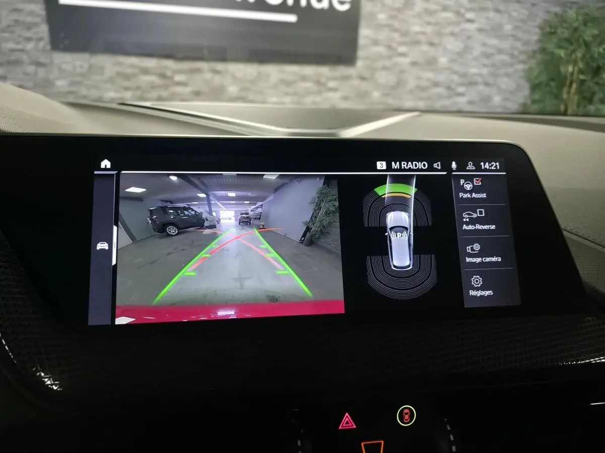 Écran central tactile montrant la caméra de recul d'une BMW Série 1 116d M Sport rouge, vue arrière avec aides au stationnement.