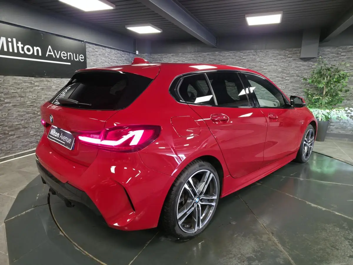 BMW Série 1 116d M Sport rouge vue 3/4 arrière droit en intérieur avec jantes alliage 18 pouces et feux LED.