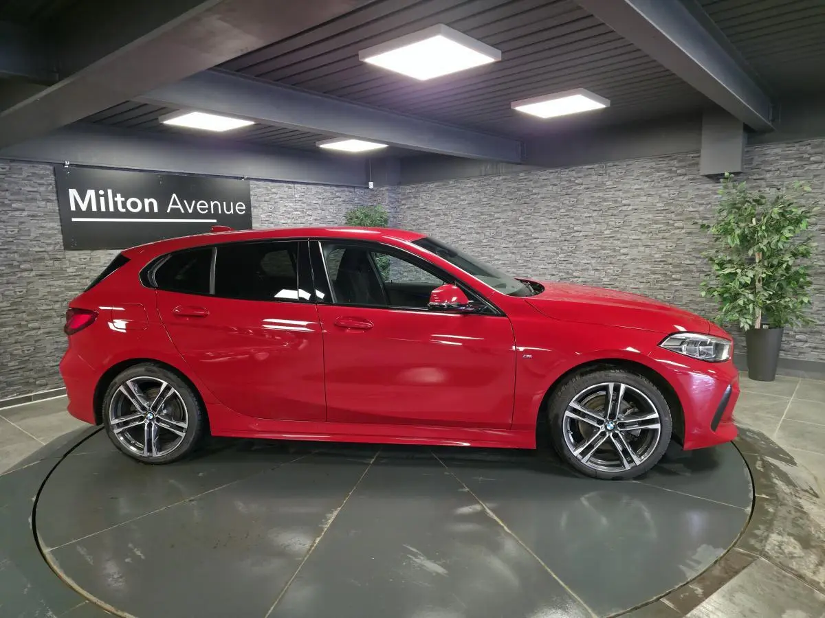 BMW Série 1 116d M Sport rouge vue de profil côté gauche, avec jantes alliage 18 pouces et détails M Sport visibles.