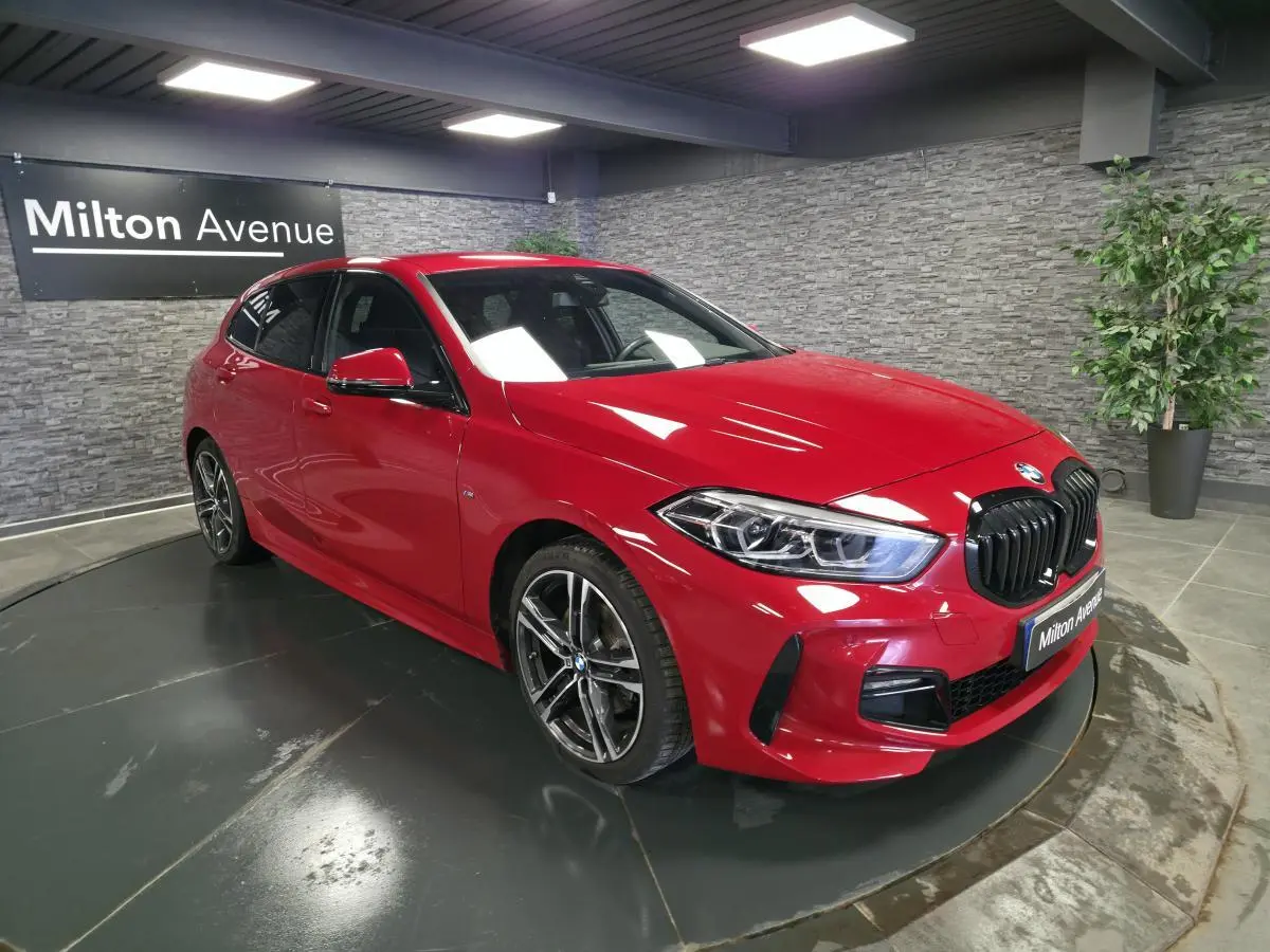BMW Série 1 116d M Sport rouge vue 3/4 avant droit, calandre noire satinée et jantes alliage 18 pouces bicolores.