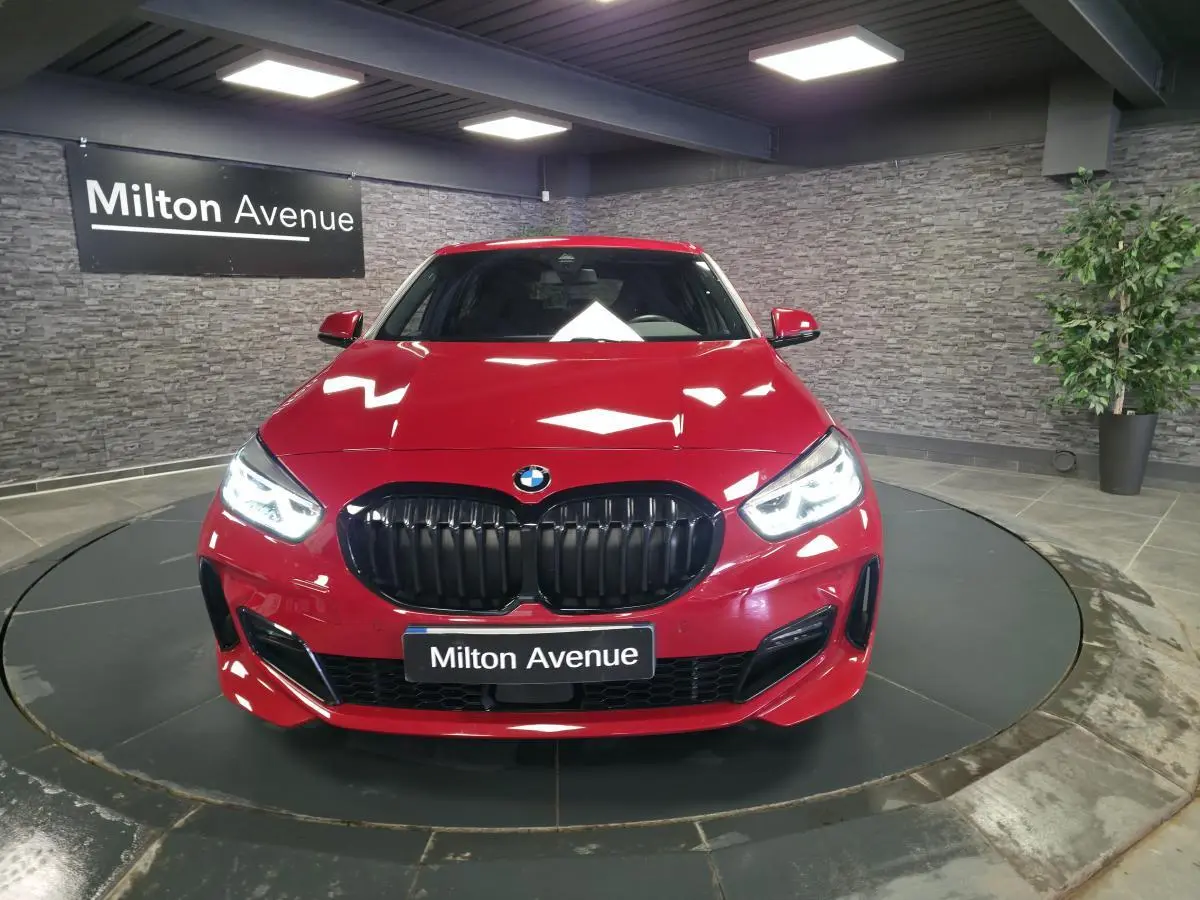Vue frontale d'une BMW Série 1 116d M Sport rouge métallisé avec calandre noire et phares LED allumés.