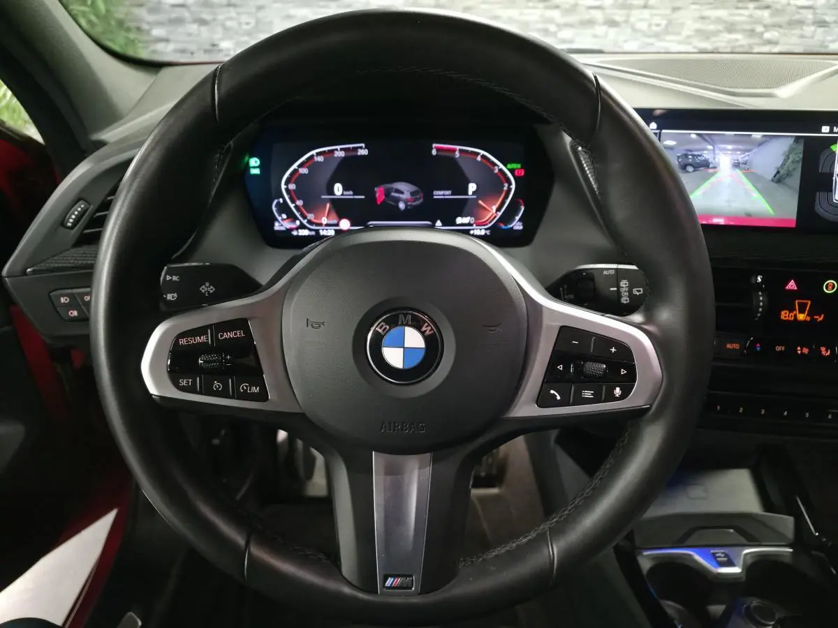 Vue centrée sur le volant M cuir noir de la BMW Série 1 116d 2024, avec tableau de bord numérique et écran de caméra de recul.