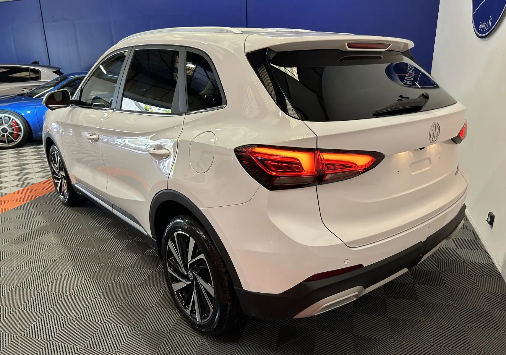 Vue 3/4 arrière droite du SUV MG ZS 1.5 Hybrid+ Dover White avec feux LED allumés en intérieur showroom.