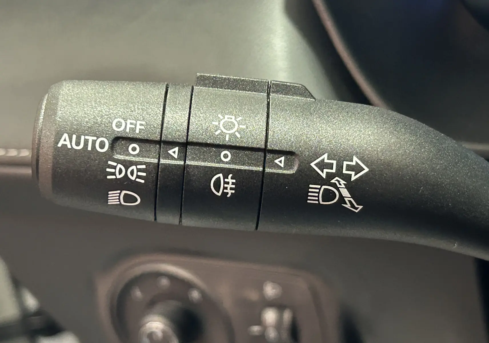 Gros plan sur la commande de phares et clignotants du MG ZS 1.5 Hybrid+ 197 Luxury en intérieur noir.