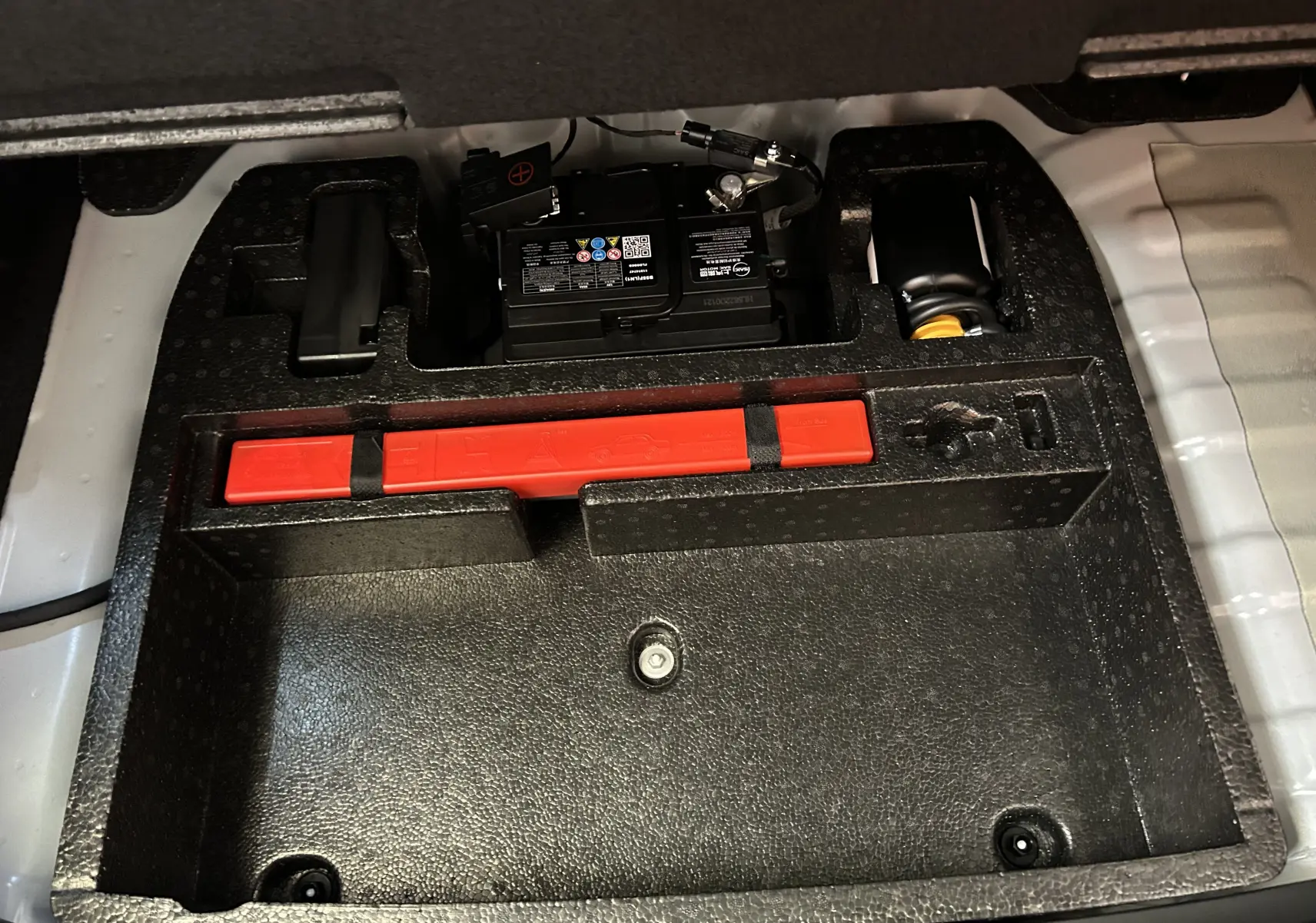 Compartiment de rangement sous plancher de coffre avec batterie et triangle de signalisation rouge du MG ZS 1.5 Hybrid+ 197 Luxury blanc.