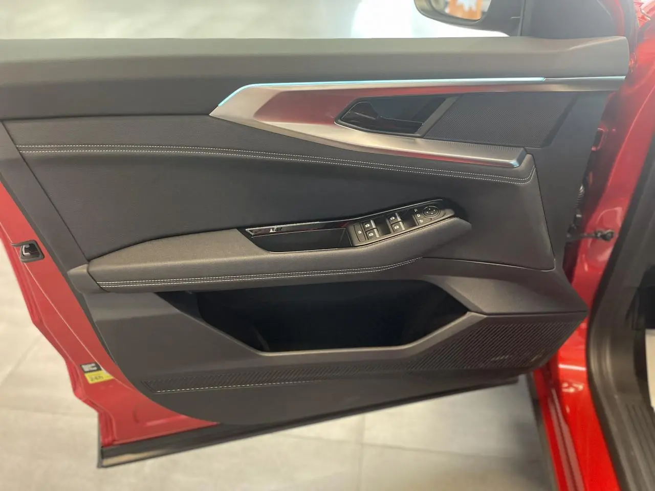 Porte avant gauche rouge avec garniture intérieure noire, surpiqûres blanches et commandes électriques des vitres.