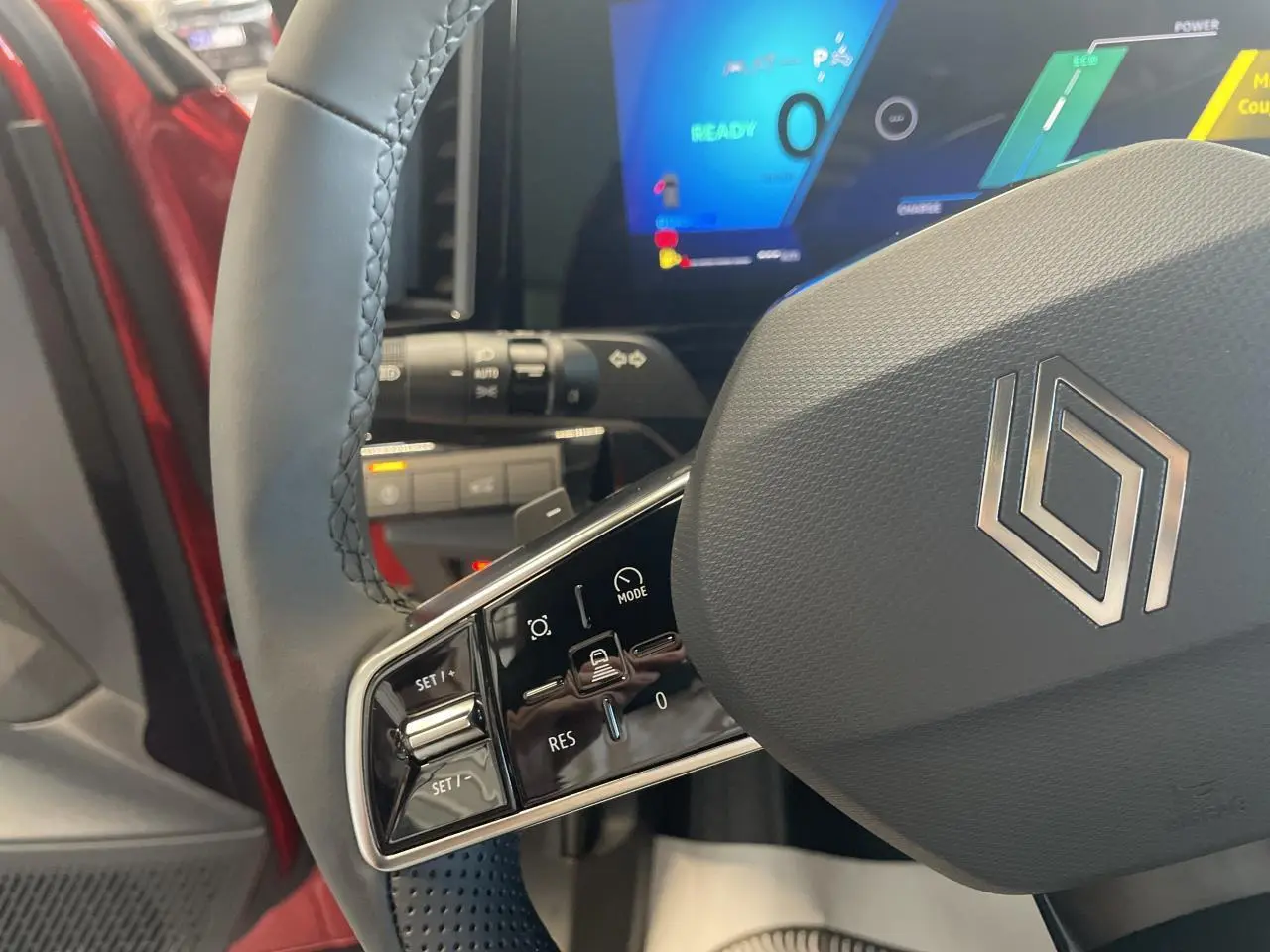 Gros plan sur le volant textile refined gris du Renault Rafale 2025 rouge, avec commandes intégrées et tableau de bord numérique.