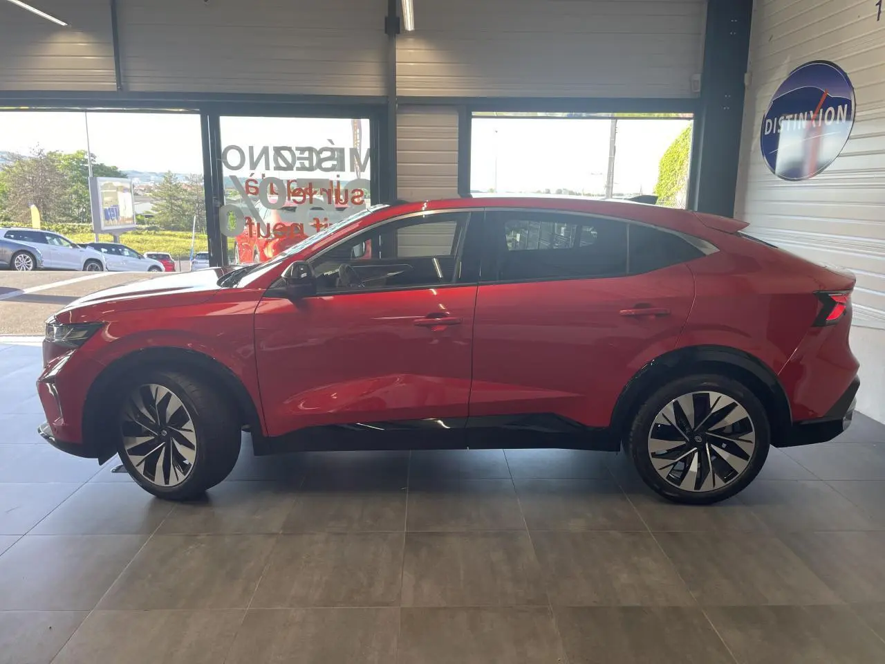 Profil côté gauche de la Renault Rafale rouge à toit noir, avec jantes alliage noires et vitres surteintées, en intérieur showroom.