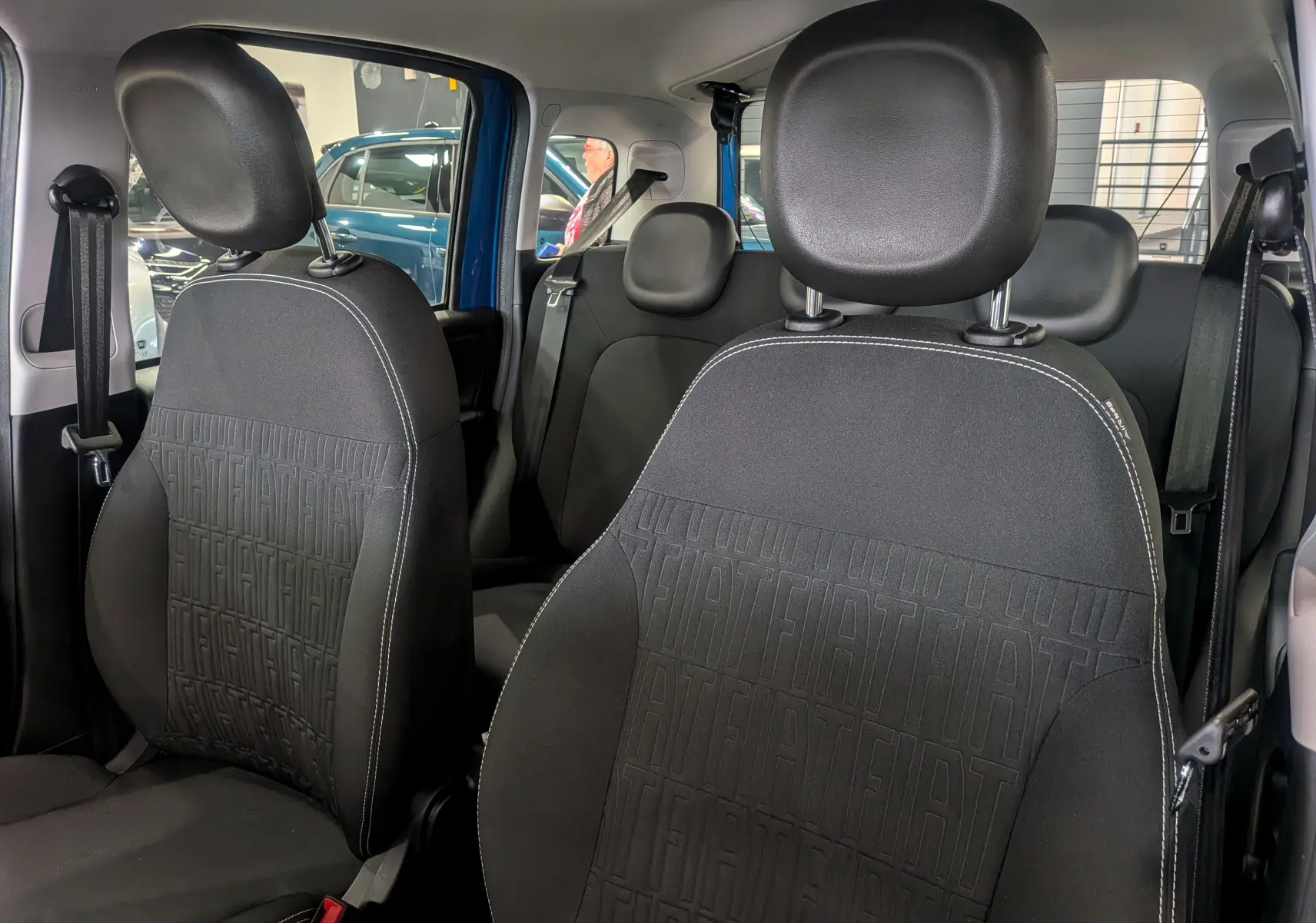 Intérieur de la Fiat Panda 1.0 Hybrid 2025, vue avant des sièges en tissu noir avec motifs FIAT embossés.