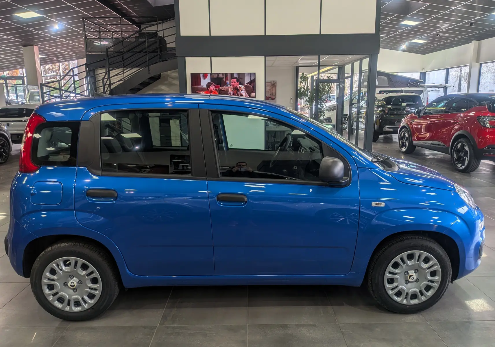 Profil latéral droit d'une Fiat Panda 1.0 70 CH Hybrid City bleu Italia en showroom, avec jantes acier et rétroviseurs noirs.