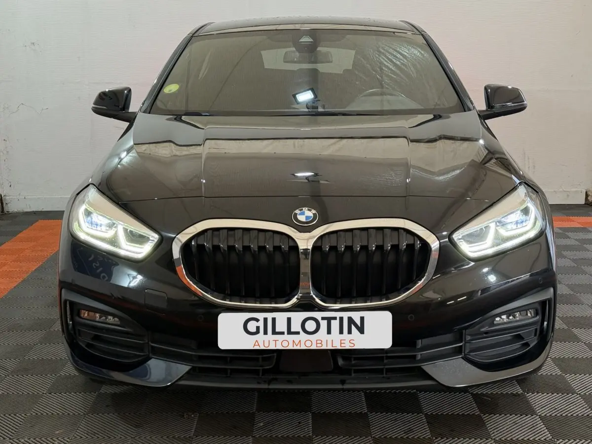 Vue avant d'une BMW Série 1 116d noire avec phares LED allumés et calandre double haricot chromée.