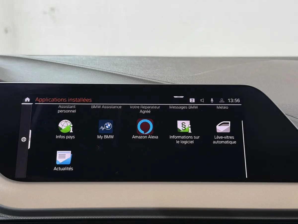 Écran tactile central affichant les applications installées dans le tableau de bord beige d'une BMW Série 1 noire.