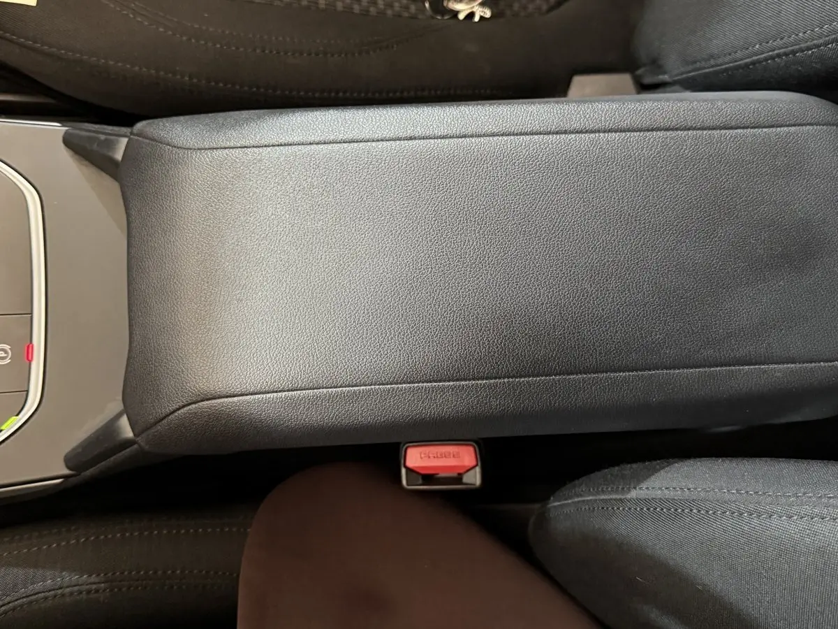 Vue rapprochée du couvercle de la console centrale noire et du bouton de ceinture rouge dans une BMW Série 1 116d DKG7 Business Design.