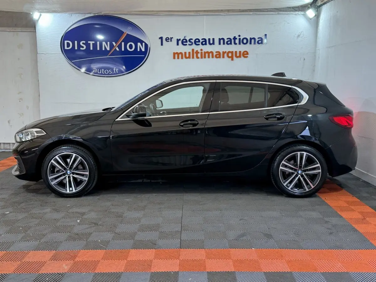 Vue de profil côté gauche d'une BMW Série 1 116d Business Design noire, avec jantes alliage et feux arrière LED visibles.