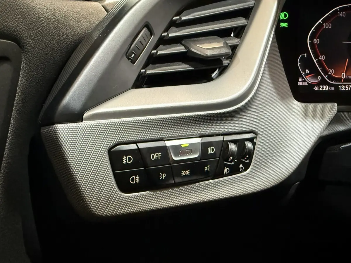 Gros plan sur le tableau de bord gris clair côté gauche de la BMW Série 1 116d, avec commandes d’éclairage et ventilation.