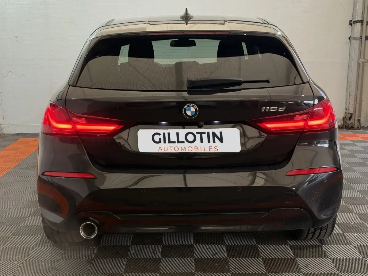 Vue arrière d'une BMW Série 1 116d noire avec feux LED allumés et sortie d'échappement visible côté gauche.