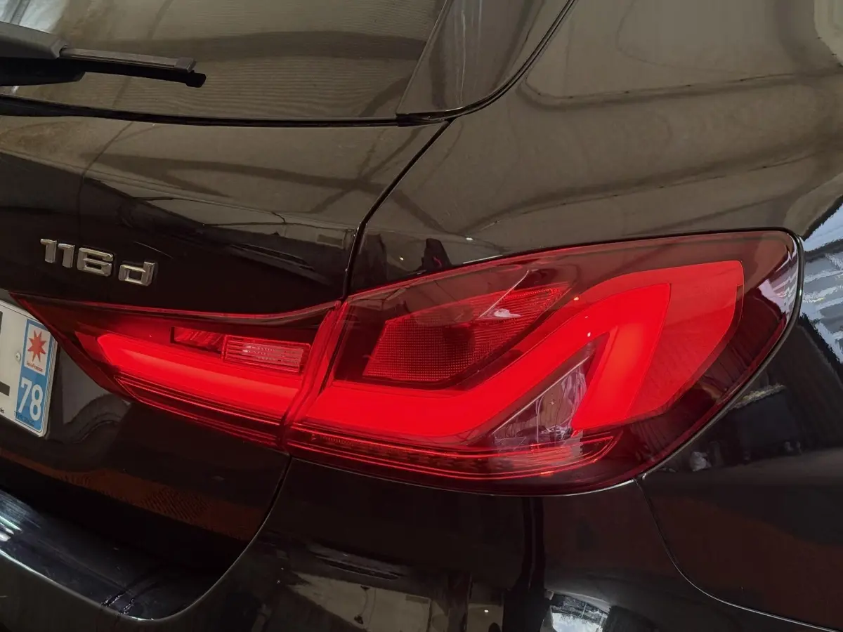 Gros plan sur le feu arrière droit rouge vif d’une BMW Série 1 116d noire, avec logo 116d visible sur le coffre.