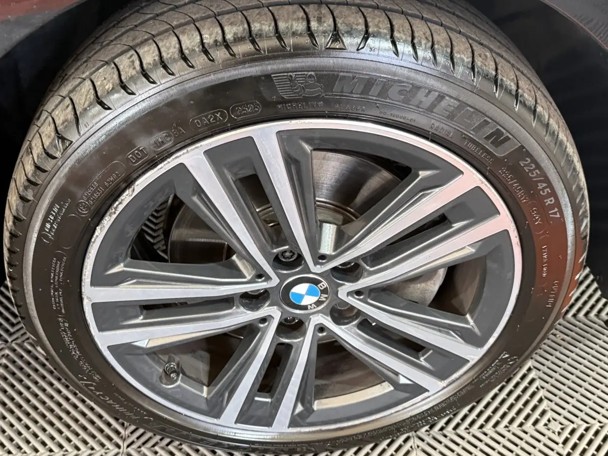 Gros plan sur la roue avant droite d’une BMW Série 1 noire, jante alliage à design étoilé et pneu Michelin.