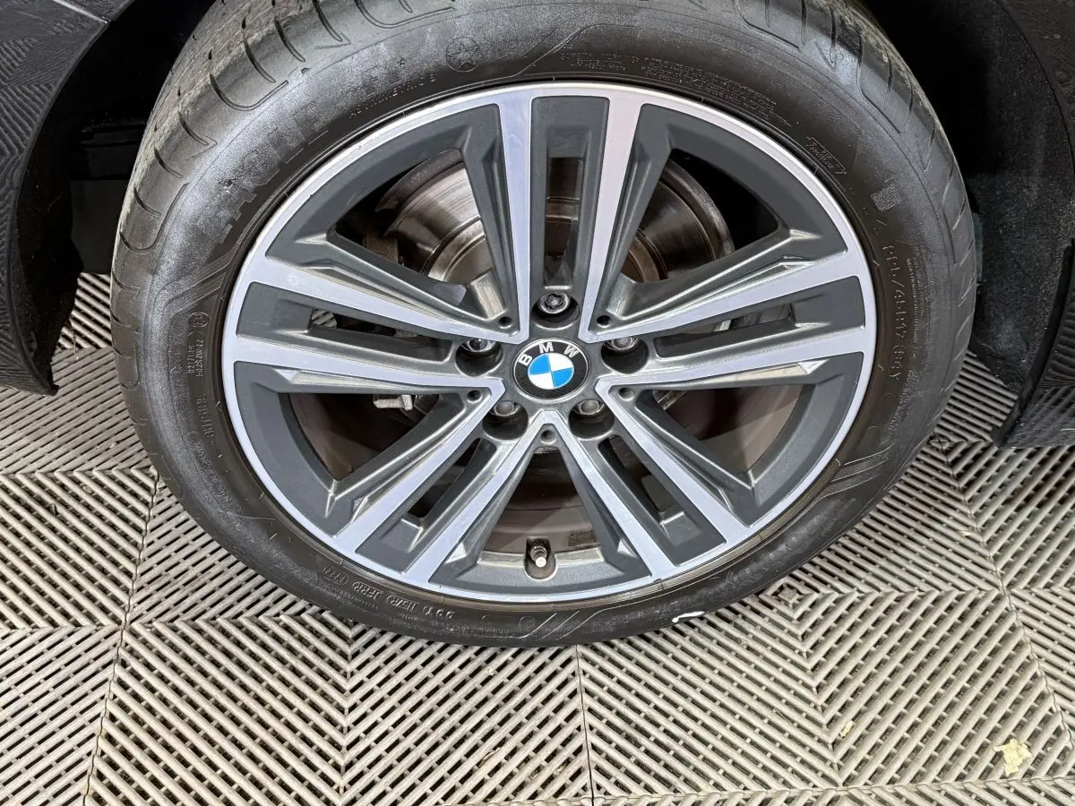 Gros plan sur la jante alliage grise avec logo BMW au centre, roue avant droite d'une BMW Série 1 noire.
