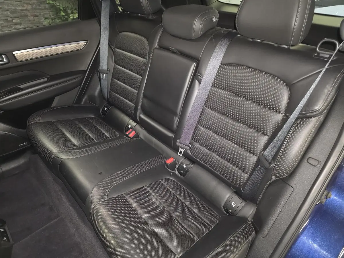 Vue intérieure des sièges arrière en cuir noir du Renault Koleos bleu, avec accoudoir central relevé et ceinture de sécurité.