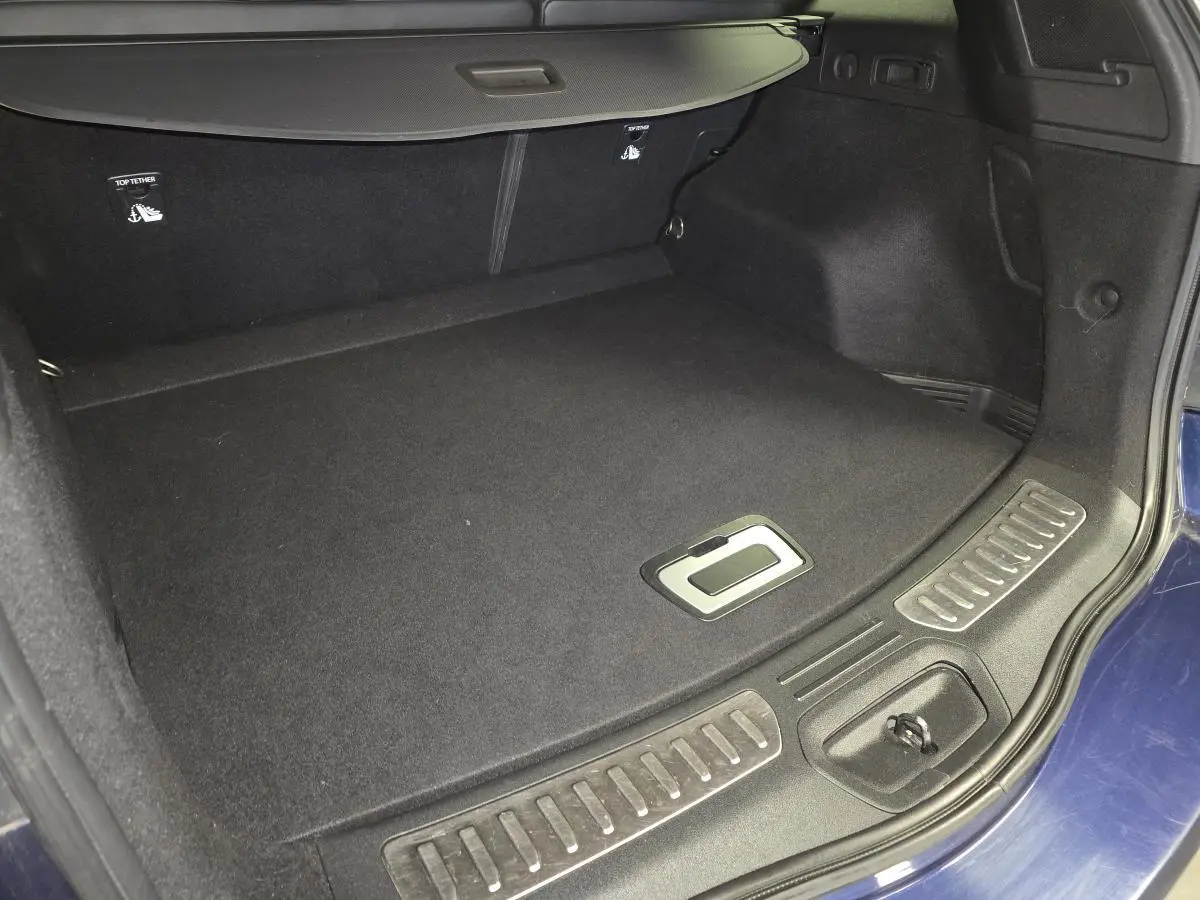 Coffre ouvert du Renault Koleos bleu, vue intérieure montrant le tapis noir et la trappe de rangement au sol.