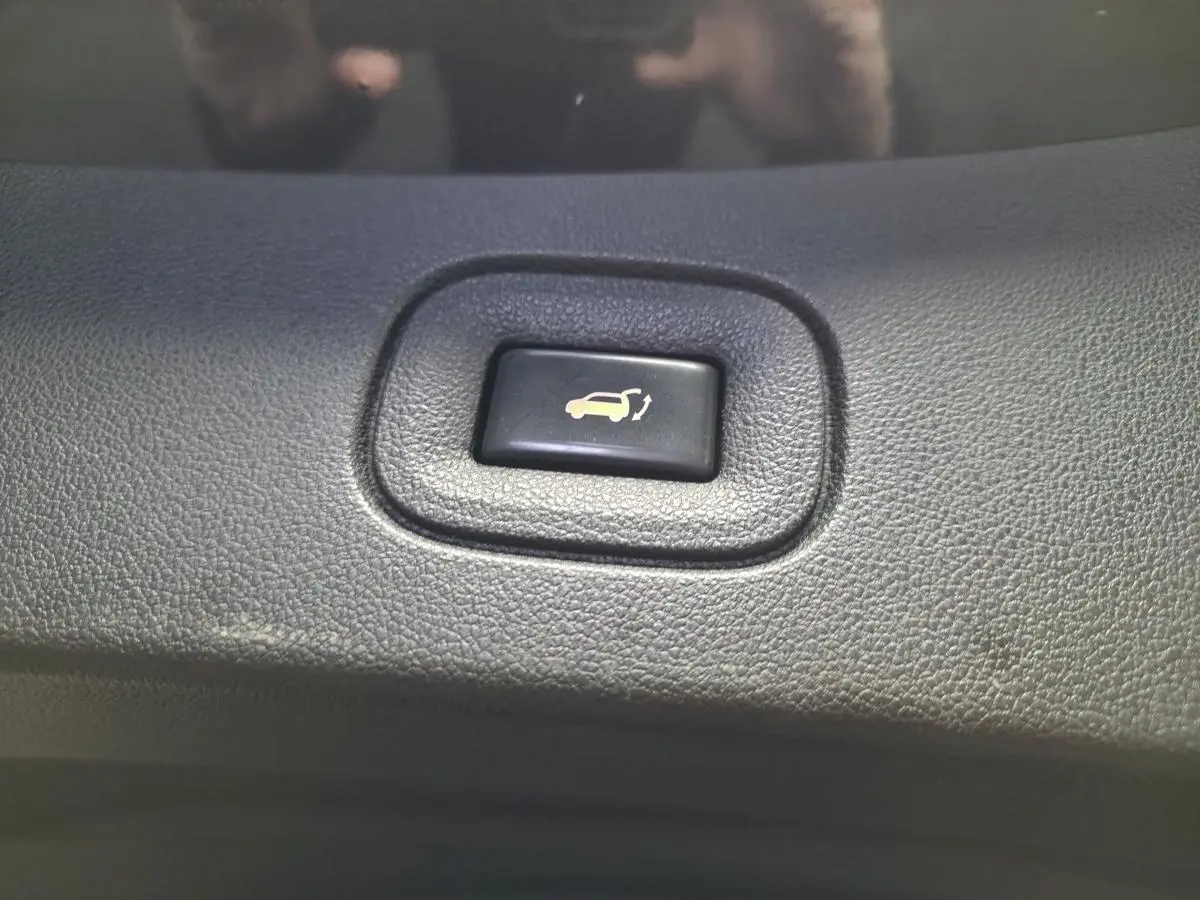 Bouton noir d'ouverture motorisée du hayon sur tableau de bord du Renault Koleos bleu de 2017, vue rapprochée.