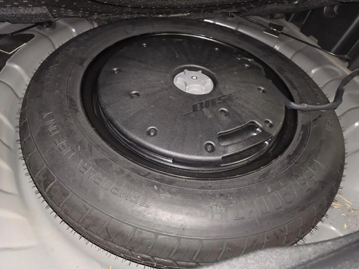 Gros plan sur la roue de secours galette noire avec caisson Bose intégré dans le coffre du Renault Koleos bleu.