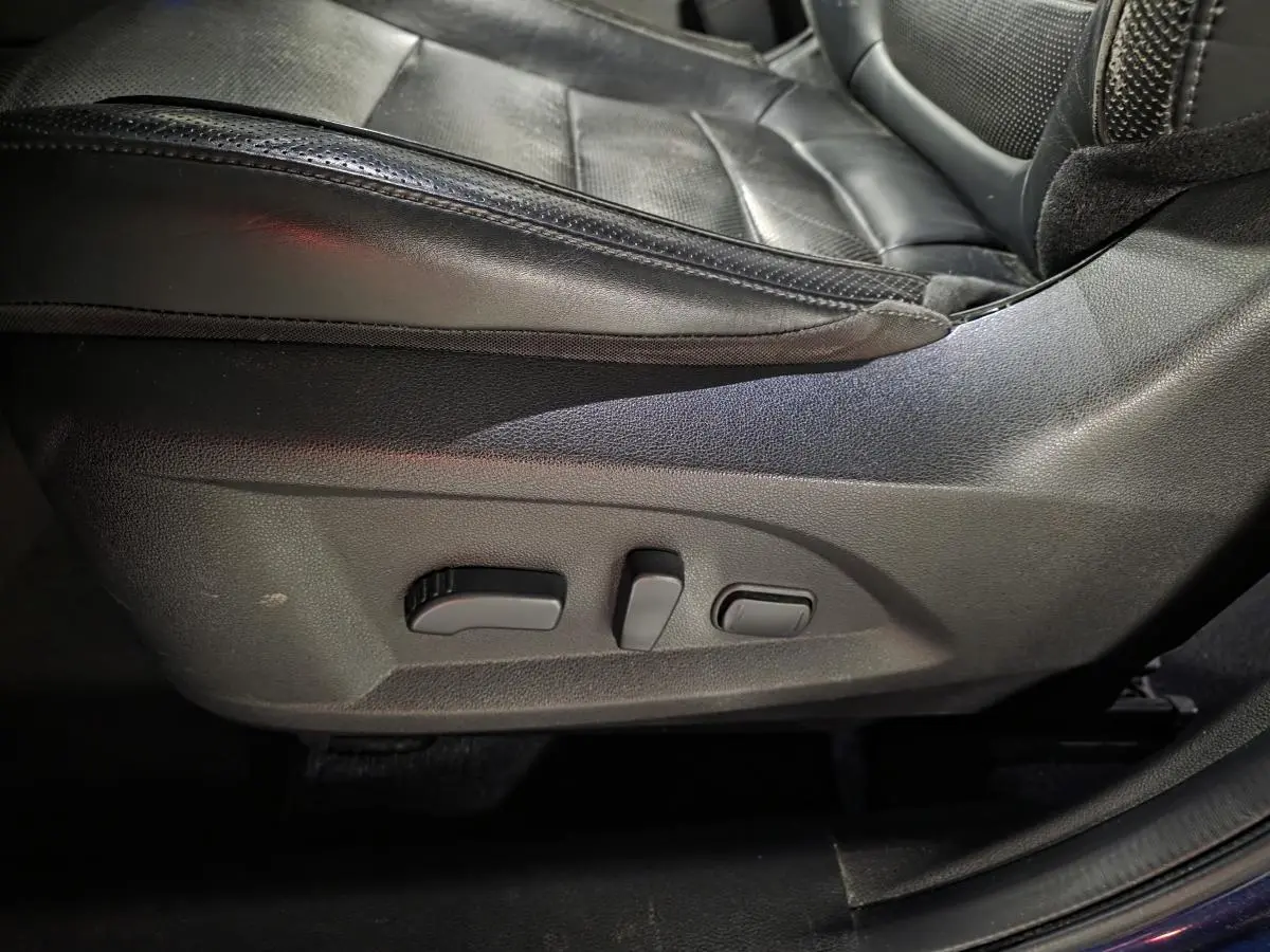 Gros plan sur les commandes électriques du siège avant gauche en cuir noir du Renault Koleos bleu de 2017.